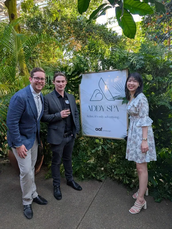 Three people posing next to an AAF Pittsburgh ADDY Awards sign at the ceremony venue